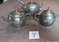 Three-piece antique pewter tea set including teapot, sugar bowl, and creamer arranged on table.