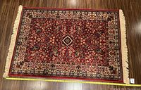 Full top view of the wool area rug displayed on wooden floor, showing design and overall condition with measuring tape.