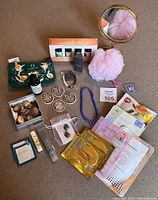 Lot overview showing vanity mirror, diffuser oils, bath pouf, facial masks, stones, and jewelry components laid out on floor