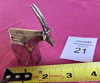 Front angled view of one silver antelope figurine showing its polished silver finish, stylized geometric body form, and long pointed horns; displayed with measuring tape showing approximately 2 inches height and length.