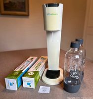 Full view of the SodaStream soda maker with two reusable soda bottles and two boxed used CO2 cartridges placed on a table.