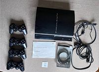 Sony PlayStation 3, four controllers, cables, paired charge cable and manuals displayed on surface.