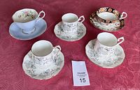 Overview of the five teacups and matching saucers displayed on a magenta tablecloth with a MaxSold lot number card.