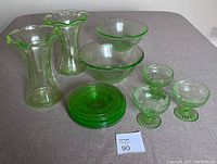 Full set of uranium glassware arranged on table showing two vases, two bowls, six plates, and three dessert bowls all fluorescent green under blue light.