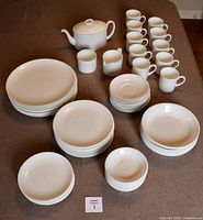 Group of all dinnerware items arranged on table: plates, bowls, cups, saucers, teapot, creamer, sugar bowl