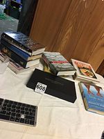 Box containing assorted books with different titles stacked and laid out on table.
