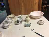 View of entire lot including pink milk glass bowl, Lenox bowls, sugar and creamer set, Navajo style bowl, small creamer with chip, Everton Creek pottery, NY dish, and pie server on table.
