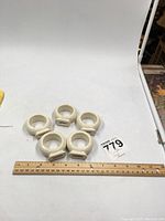Five off white ceramic napkin rings arranged on white surface with ruler for size reference.