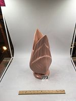 Full view of the pink ceramic vase showing its fluted petal-like design and rounded base, set against a white background with a ruler for scale.