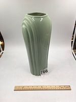 Front view of a tall green ceramic Art Deco style vase showing smooth glossy finish and vertical grooves on the sides, with a ruler for scale.