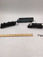Photo of the three items including two steam locomotives and a blue and silver passenger car along with a ruler for scale.