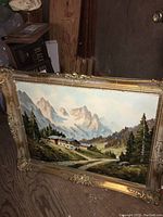 Full view of the framed oil painting showing the mountain landscape and chateau