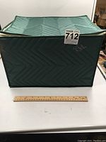 Front view of green quilted storage case with ruler for size reference, showing rectangular shape and padded fabric.