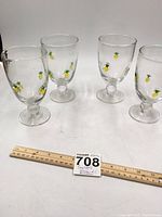 Four clear glass goblets decorated with small yellow pineapples with green leaves around the bowl, with a ruler for size reference.