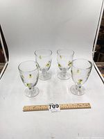 Four clear glass goblets arranged on white background with ruler showing size. Each glass has small yellow pineapples with green leaves painted around the bowl.