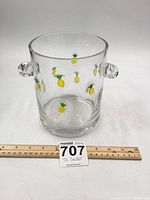 Full view of clear glass ice bucket with small yellow and green pineapples decorating the surface. Two rounded handles visible.