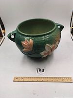 Front view of the large green Roseville magnolia floor bowl featuring pink floral raised decorations and side handles, showing size relative to 12 inch ruler.