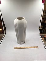 Front view of tall white ceramic vase on white background with ruler for scale