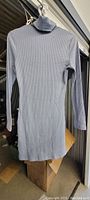 Blue long-sleeved dress with turtle neck hanging on a hanger, showing ribbed texture and fitted shape.