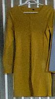 Yellow long sleeved dress hanging on a door shown with visible ribbed knit texture and round neckline.