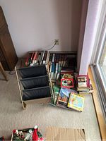 Overview of assorted books organized on the floor next to a window and a black leather and brass magazine rack.