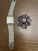 The watch and brooch together on a wooden surface showing size and details.