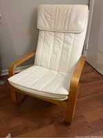 Side angle of Poang style chair showing light wood frame and cream cushioned seat and back with curved wooden arms.