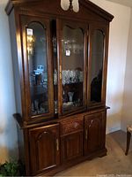 Full frontal view of tall wooden china cabinet with glass upper doors showing decorative carved wooden details