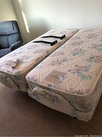 Two single electric beds with floral mattresses, remotes on top and black metal frame brackets