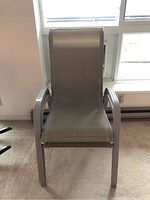 Front view of one metal framed patio chair with mesh seating under a window.
