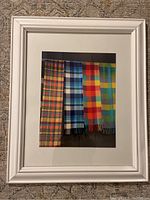 White framed photo featuring four colorful plaid scarves hung vertically