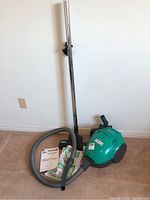 Samsung green vacuum cleaner with hose, metal extension wand, and cleaning head shown assembled and resting on carpet.