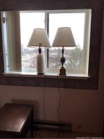 Both lamps side by side on a windowsill, showing respective finishes and lamp shades