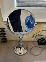 Single vanity mirror on table with round reflective surface, chrome swivel stand, and weighted round base