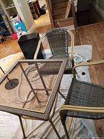 Bar patio furniture set with glass-top table and 2 wicker chairs on a protective cloth indoors