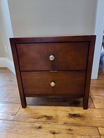 Front view of the brown nightstand showing two drawers with silver knob handles.