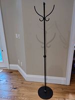 Full view of black metal coat rack standing on wooden floor against beige wall.