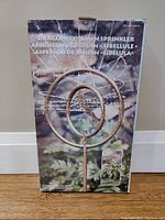 Front of the box showing the dragonfly lawn sprinkler image and product name in multiple languages.
