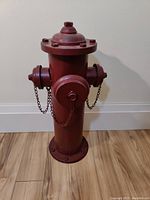 Front view of rustic red fire hydrant decoration on wooden floor against white wall.