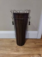 Front view of rustic tall hammered metal umbrella holder with wire scalloped rim and side tassels.