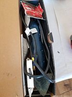 View of Ryobi detail sander in box with power cord and sanding sheets.