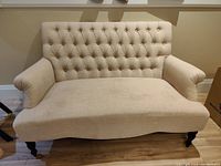 Full view of white loveseat sofa showing shape and tufted back.