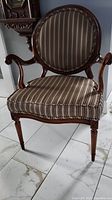 Front view of vintage wooden accent chair with beige, brown and black striped upholstery on seat and rounded backrest.