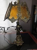 Full view of the lamp showing the amber stained glass shade with ornate metal trim and cupid base for overall shape and condition.