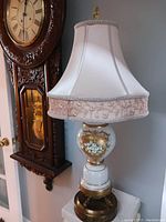 Full view of the lamp showing the white silk lampshade with embroidered floral band and the glass base with gold detailing.