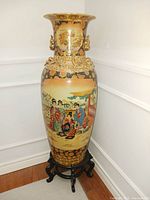 Front full view of the large Moriage Satsuma vase placed on the rosewood stand, showing detailed painted traditional Japanese scenes with raised gold embellishments.