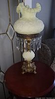 Full view of lamp on wooden surface showing milk glass shade, bronze base and crystal drops
