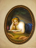 Oval porcelain miniature painting of a reclining woman reading a book, mounted in an oval bronze ormalou frame with detailed edging.