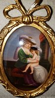 Close-up image of the front of the oval porcelain painting showing the woman and child in period attire in the gold-tone bow decorated wooden frame