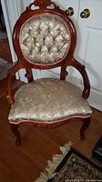 Front view of the chair showing carved wood frame, tufted upholstered backrest, padded arms, and floral patterned seat cushion.